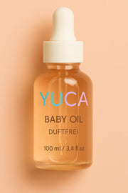YUCA Baby Oil in einer transparenten Glasflasche mit weißer Pipette vor rosafarbenem Hintergrund – duftfreies Pflegeöl für Babys, 100 ml